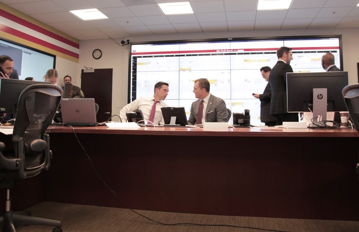 Shanahan and Lynch discuss strategy while Marathe (left) works the phones and Peters and Mayhew (right) review the board.
